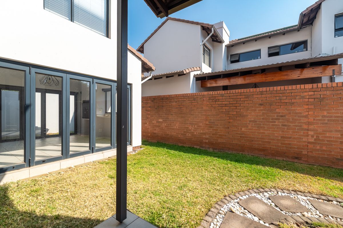 A private rear garden featuring a paved path, lawn, and a covered patio area with modern bi-fold doors leading into the home.