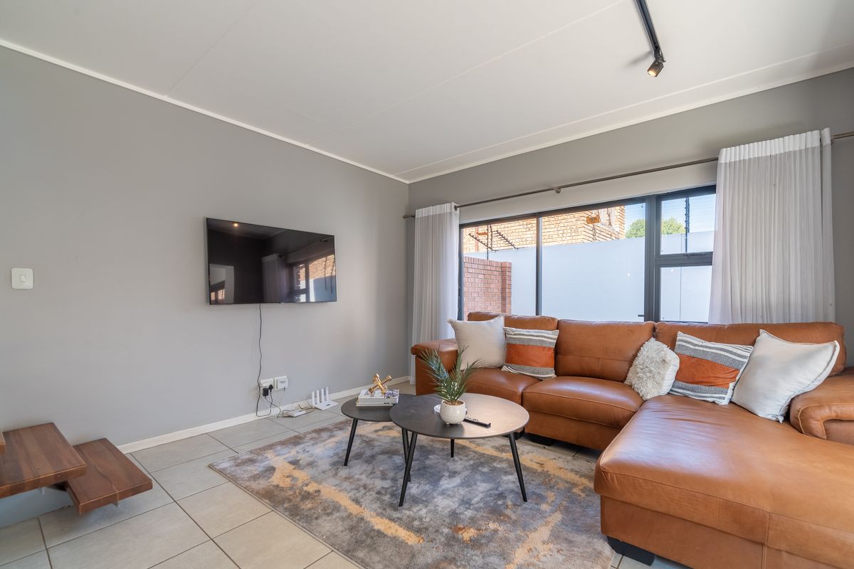 A bright and well-maintained living room featuring neutral grey walls, tiled flooring, and large windows that provide ample natural light.