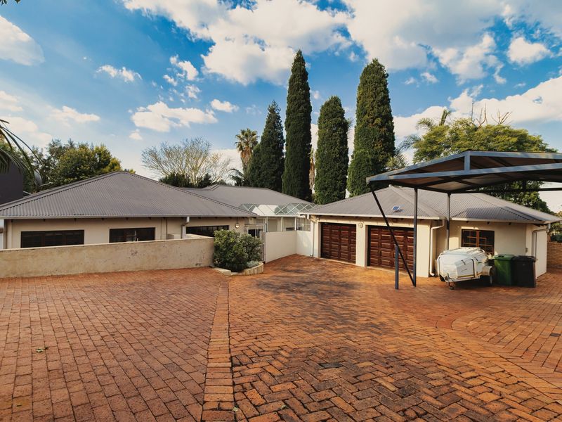 Front exterior view featuring a spacious paved driveway, double garage, and a covered carport area with established landscaping.