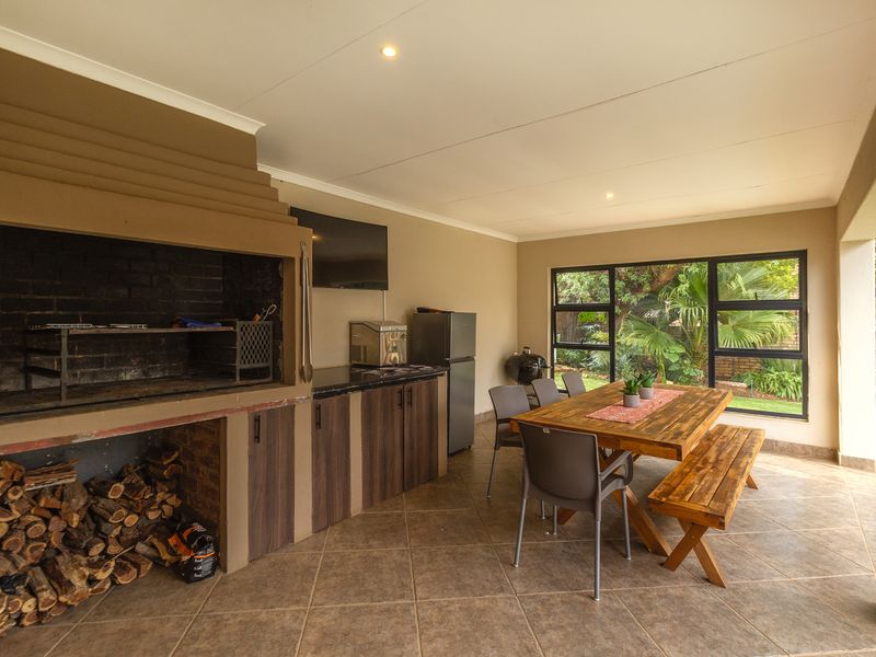 Covered patio featuring a built-in braai, granite prep area, and tiled flooring, overlooking the garden through large aluminium-framed windows.