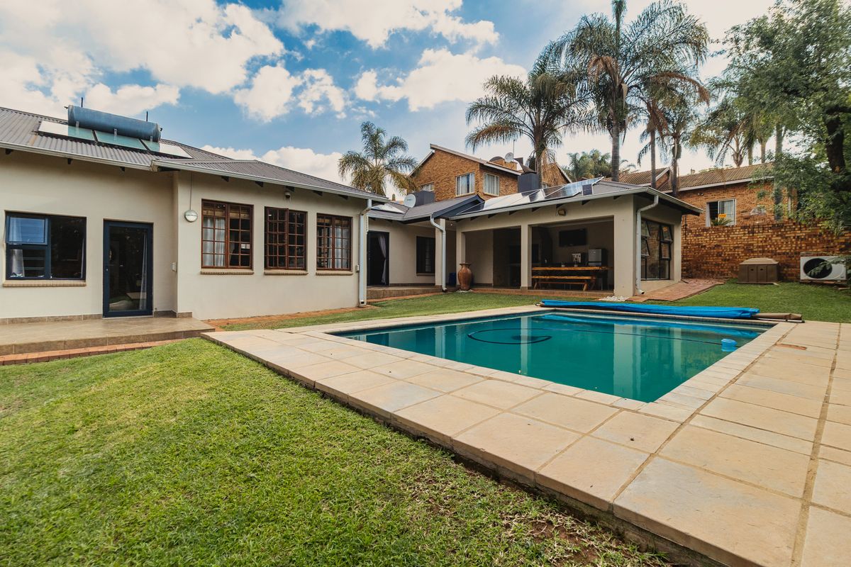 Rear exterior view featuring a swimming pool, paved surround, covered patio area, and integrated solar energy systems on the roof.