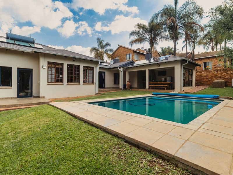 Rear exterior view featuring a swimming pool, paved surround, covered patio area, and integrated solar energy systems on the roof.