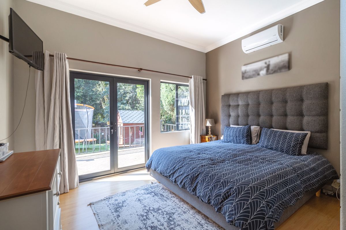 A well-maintained bedroom featuring laminate flooring, crown molding, a split-system air conditioner, and direct access to an outdoor patio area.