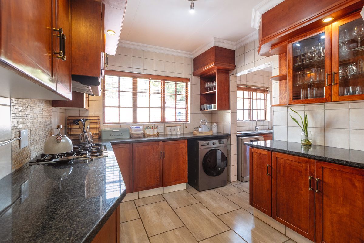 A well-maintained kitchen featuring warm wooden cabinetry, granite countertops, a gas hob, and integrated laundry appliances with a classic tiled finish.