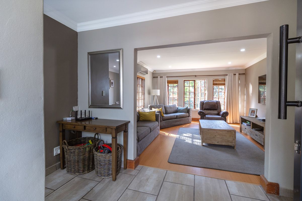 A well-maintained living room featuring laminate flooring, recessed lighting, and crown molding, seamlessly connected to an entry area with tiled floors.