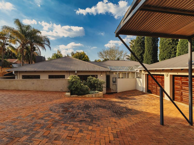 Front exterior view of the property featuring a spacious brick-paved driveway, double garage, and a covered carport area.