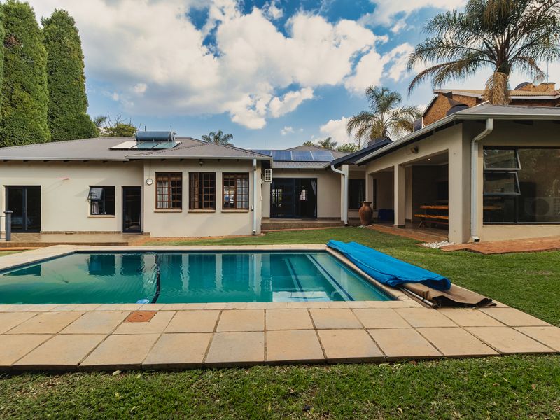 A well-maintained rear garden featuring a swimming pool, covered patio area, and integrated solar energy systems on the roof.