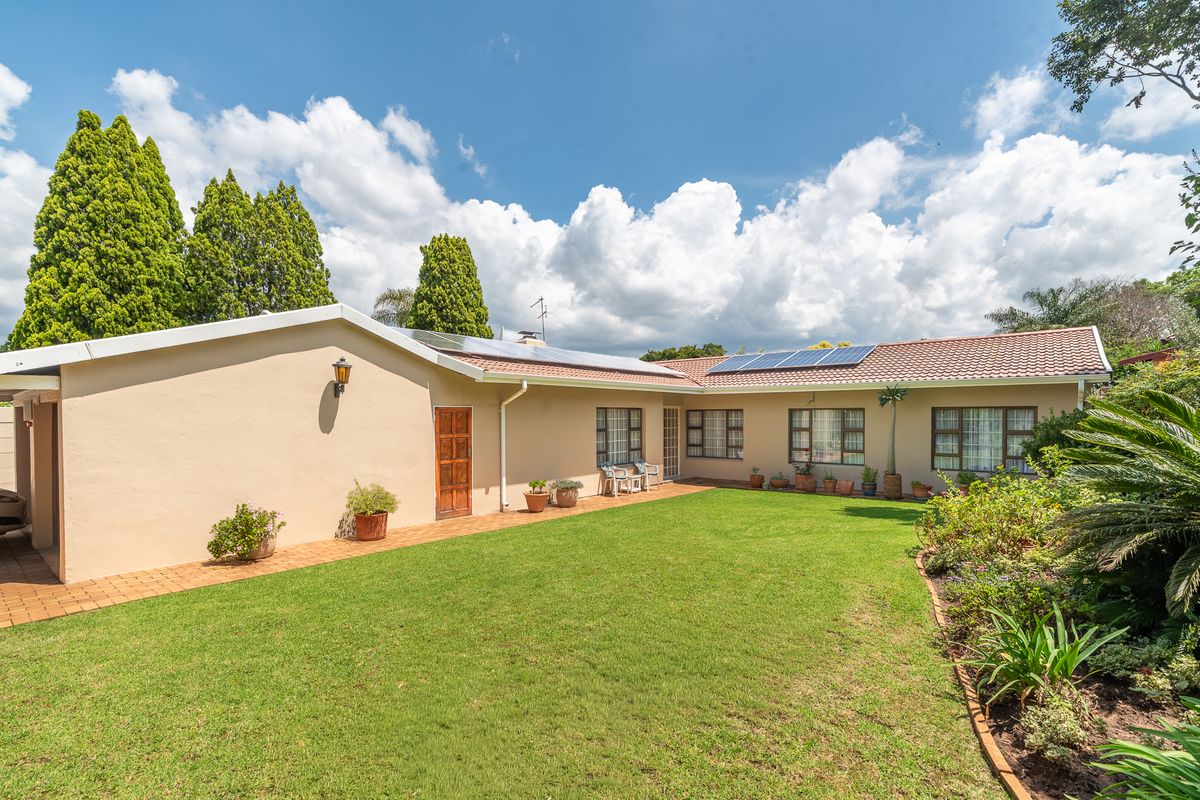 A well-maintained rear exterior view of the house featuring a spacious lawn, paved walkway, and solar panels installed on the tiled roof.