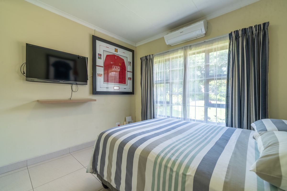 A well-maintained bedroom featuring tiled flooring, a split-system air conditioner, and a large window providing natural light.