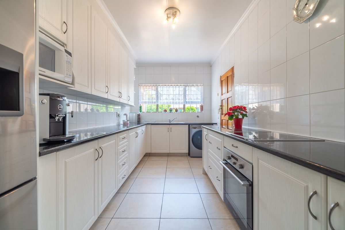 A well-maintained galley-style kitchen featuring white cabinetry, dark granite countertops, integrated appliances, and tiled finishes throughout.