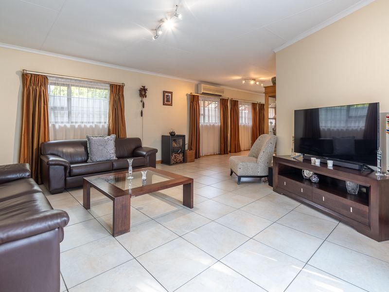 Spacious living room featuring neutral tiled flooring, coved ceilings, and an integrated air conditioning unit, offering a comfortable and well-maintained living space.
