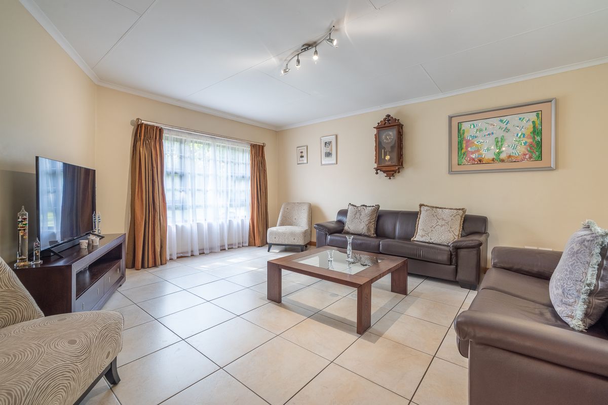 A spacious living room featuring neutral tiled flooring, ample natural light from a large window, and modern ceiling-mounted track lighting.