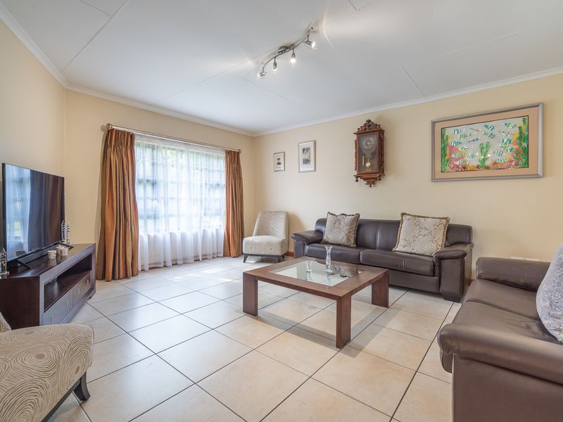 A spacious living room featuring neutral tiled flooring, ample natural light from a large window, and modern ceiling-mounted track lighting.