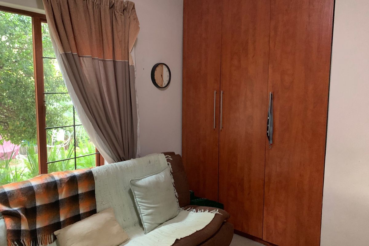 A bedroom featuring floor-to-ceiling built-in wooden cupboards and a window with security bars overlooking the garden.