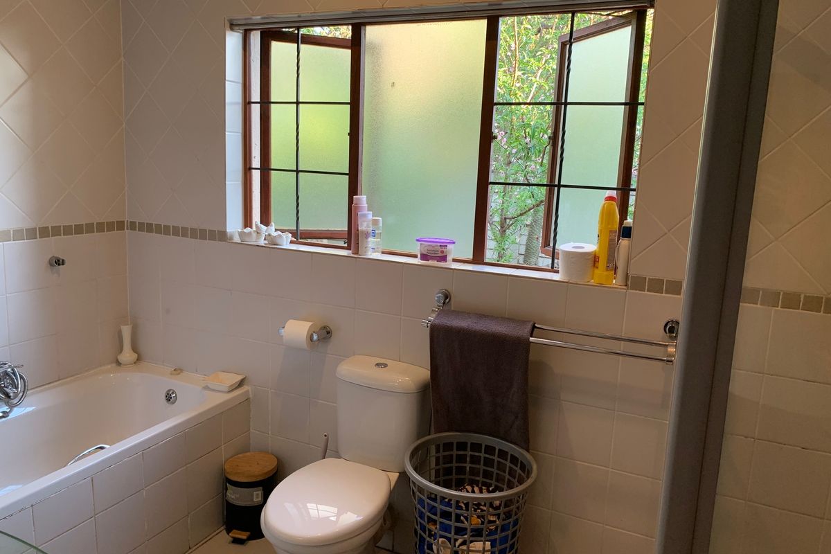 A functional bathroom featuring a built-in bathtub, toilet, and tiled finishes, with a window providing natural light and ventilation.