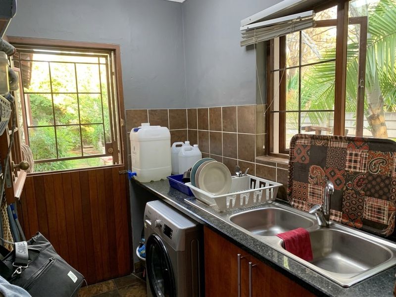 Functional scullery area featuring a double stainless steel sink, granite countertops, tiled backsplash, and a wooden stable door leading to the garden.
