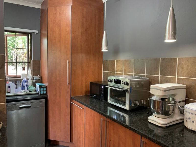 A functional kitchen featuring wood-finish cabinetry, dark granite countertops, a tiled backsplash, and modern pendant lighting.