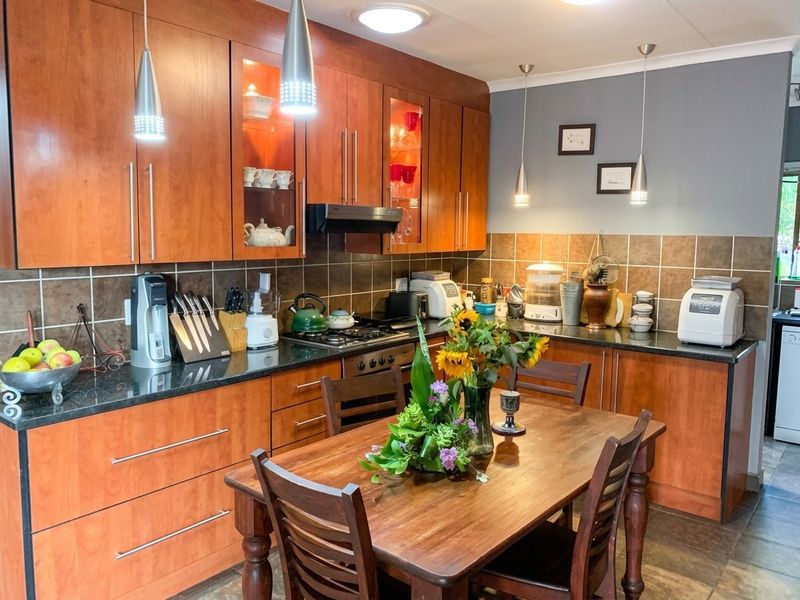 An open-plan kitchen featuring warm wooden cabinetry, granite countertops, a gas hob with extractor, and a tiled backsplash, seamlessly integrated with a dining area.