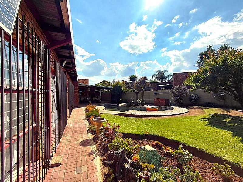 Outdoor area featuring a swimming pool, brick paved walkway, and landscaped garden with established trees and perimeter walling.