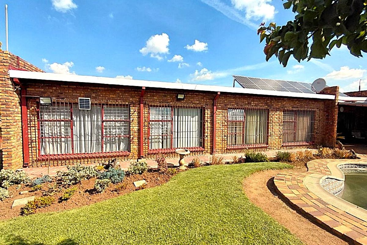Rear view of the property featuring a face brick facade, security bars, solar panels, and a swimming pool set within a landscaped garden.