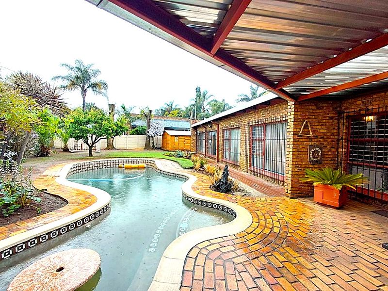 Outdoor pool area featuring a curved swimming pool, brick paved surround, and a covered patio area attached to the face brick house.