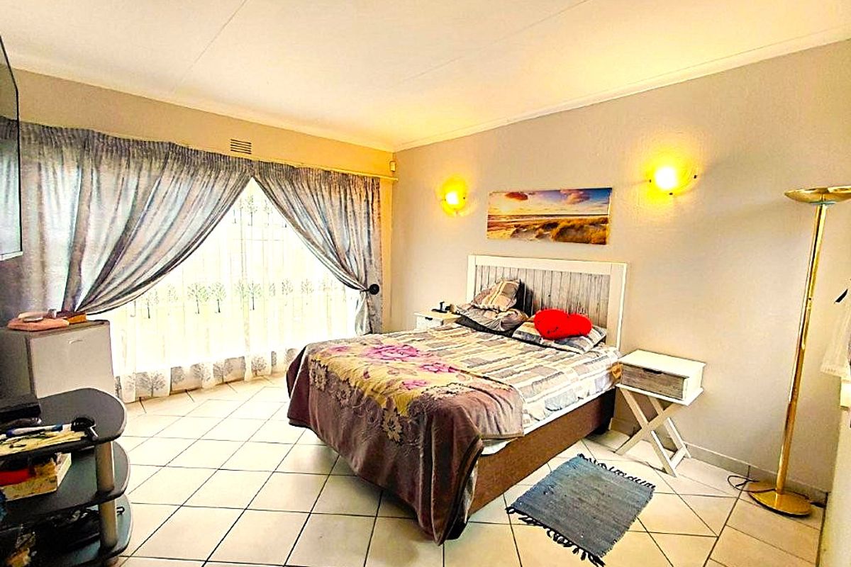 A bedroom featuring tiled flooring, wall-mounted lighting, and large windows with curtain rails, providing a functional space with neutral wall finishes.