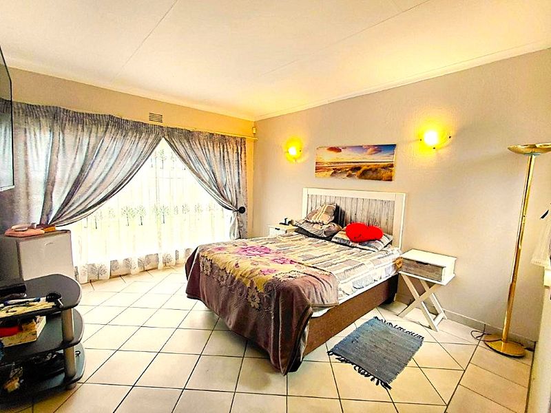 A bedroom featuring tiled flooring, wall-mounted lighting, and large windows with curtain rails, providing a functional space with neutral wall finishes.
