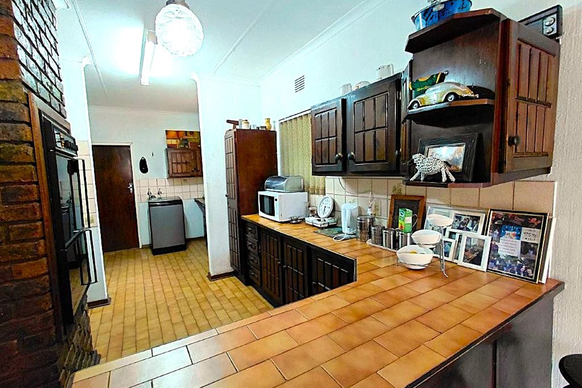 A dated kitchen featuring dark wooden cabinetry, tiled countertops, and a brick feature wall, offering potential for a modern renovation.