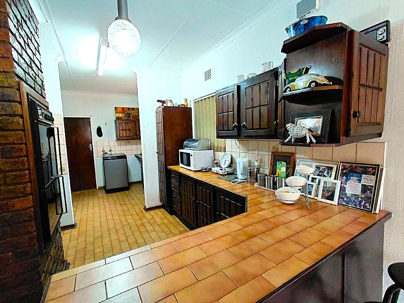 A dated kitchen featuring dark wooden cabinetry, tiled countertops, and a brick feature wall, offering potential for a modern renovation.