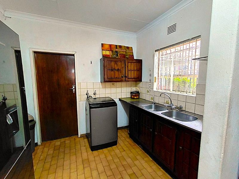 Functional laundry area featuring double stainless steel sinks, built-in wooden cabinetry, tiled splashbacks, and secure window bars.