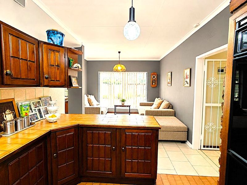 Open plan kitchen and living area featuring traditional wooden cabinetry, tiled countertops, and neutral wall finishes with direct access to a secure entrance.