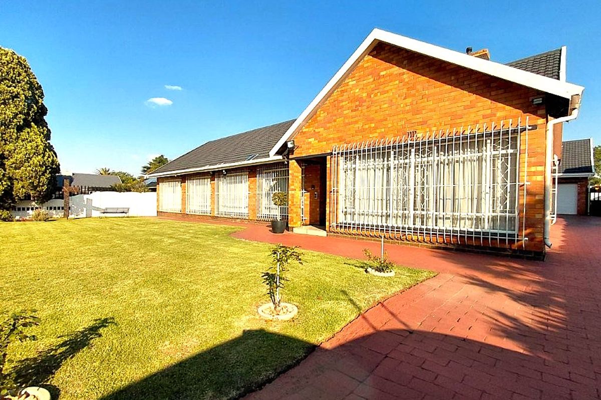 Rear view of a brick house featuring a well-maintained lawn, paved walkway, and security bars on the windows.