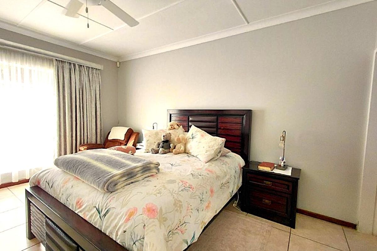 A well-lit bedroom featuring tiled flooring, a ceiling fan, and large windows with curtains, providing a comfortable and functional living space.