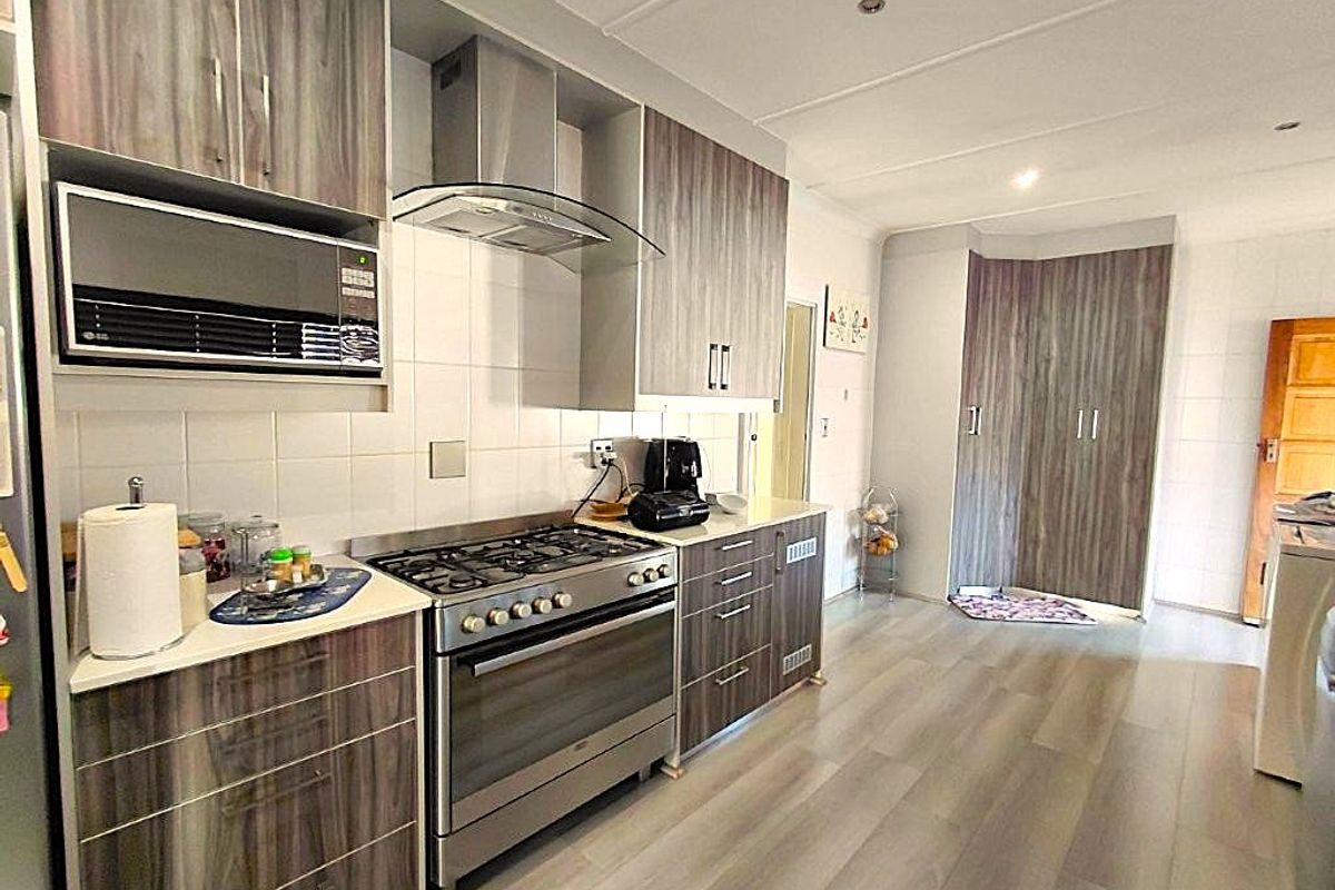 Modern kitchen featuring wood-grain cabinetry, a stainless steel gas stove with extractor fan, built-in microwave, and durable laminate flooring.