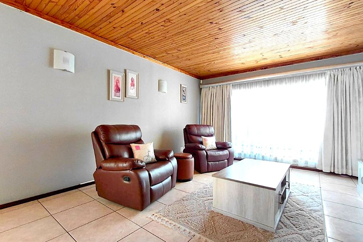 A comfortable living room featuring a warm timber tongue and groove ceiling, neutral wall finishes, and large windows that provide ample natural light.