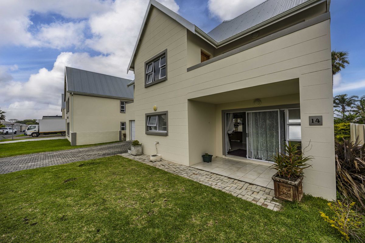 Rear view of a modern townhouse featuring a paved patio, sliding glass doors, and a well-maintained lawn area.