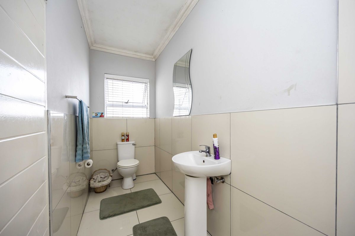 A functional guest bathroom featuring a pedestal basin, toilet, and neutral wall and floor tiling.