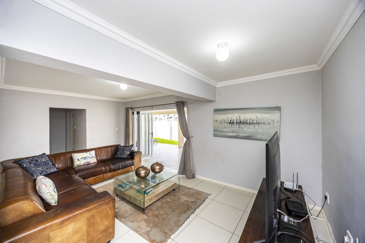 Spacious living room featuring neutral tiled flooring, crown molding, and large sliding glass doors providing direct access to the outdoor patio area.
