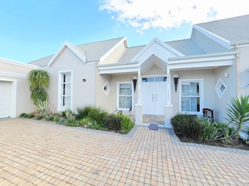 A well-maintained front elevation featuring a paved driveway, double garage, and a welcoming entrance with modern exterior lighting and landscaped garden beds.