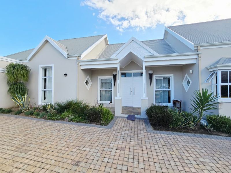 A well-maintained front facade featuring a paved driveway, double entrance doors, and a gabled roofline with established garden beds.