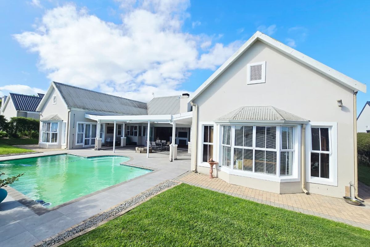 Rear view of the house featuring a swimming pool, paved patio area, and a well-maintained lawn with bay window architectural details.