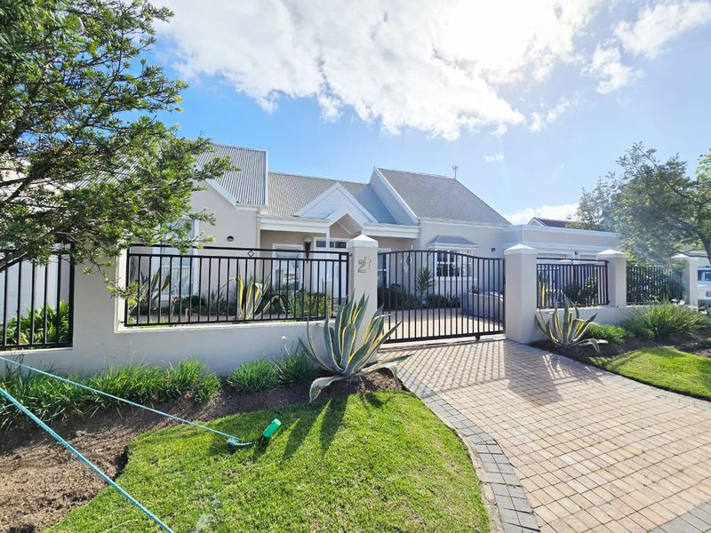 Front elevation of a well-maintained house featuring a paved driveway, secure metal perimeter fencing, and a sliding gate.