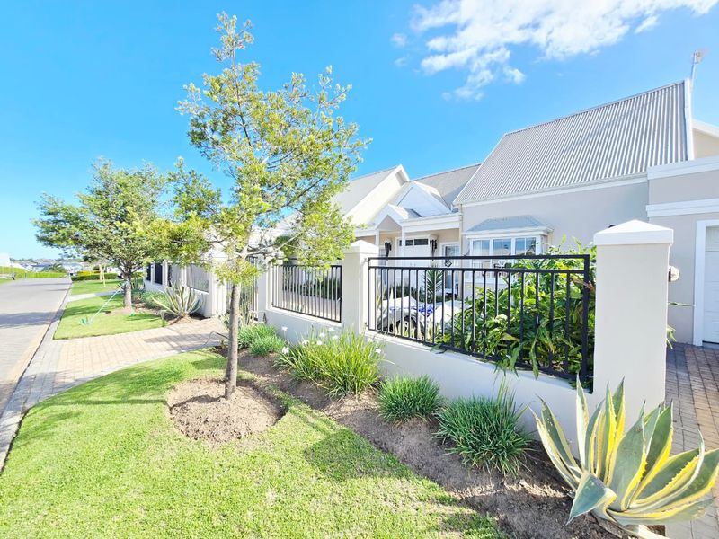 A well-maintained front exterior view featuring a paved driveway, landscaped garden, and secure metal perimeter fencing with a clean masonry boundary wall.