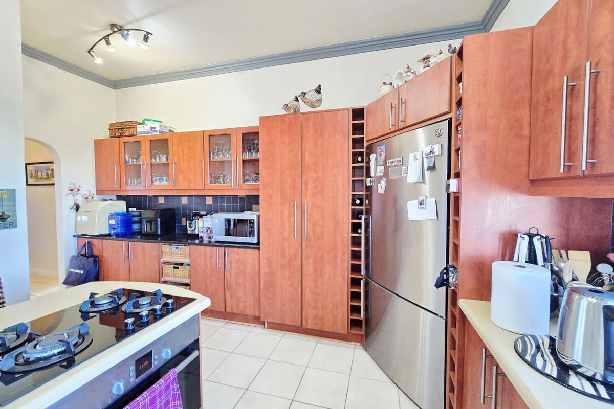A functional kitchen featuring wooden cabinetry, a central island with a gas hob, built-in oven, and tiled flooring.