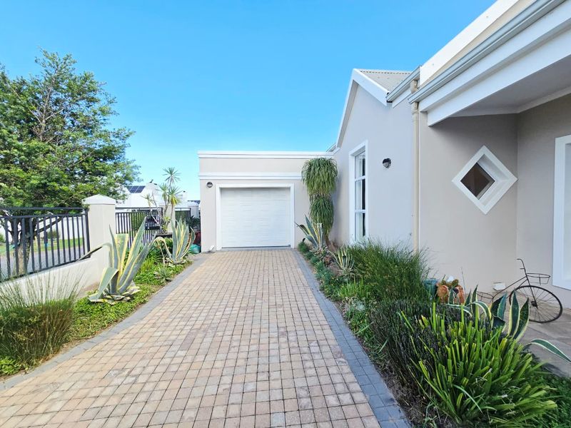 Front view of the property featuring a paved driveway, single garage, and landscaped garden beds along the exterior wall.