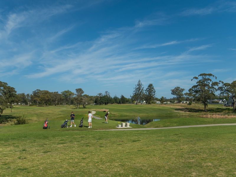 A scenic view of a well-maintained golf course featuring lush green fairways, mature trees, and a small water hazard.