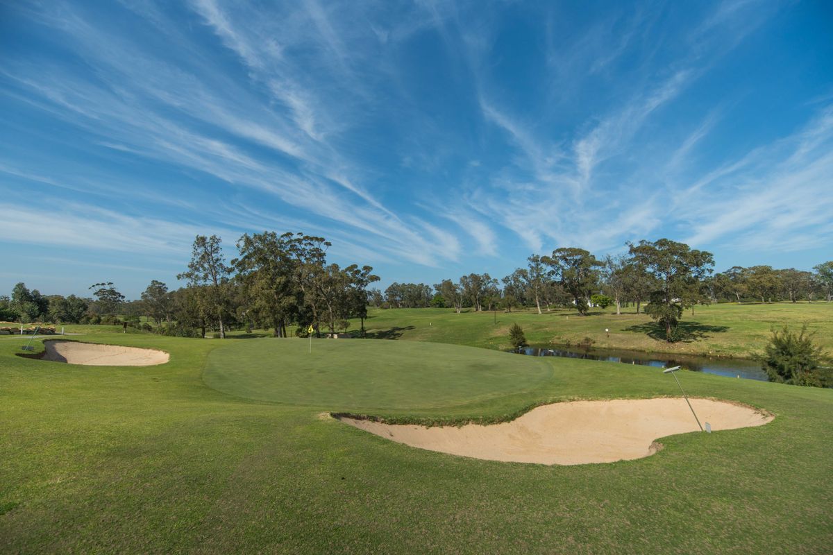 A scenic view of a well-maintained golf course featuring a putting green, sand bunkers, and a small water hazard.