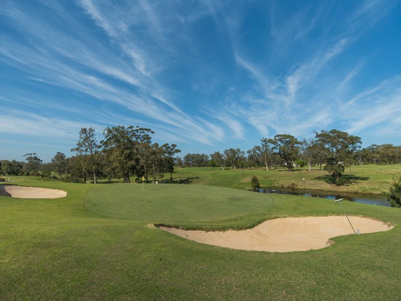 A scenic view of a well-maintained golf course featuring a putting green, sand bunkers, and a small water hazard.