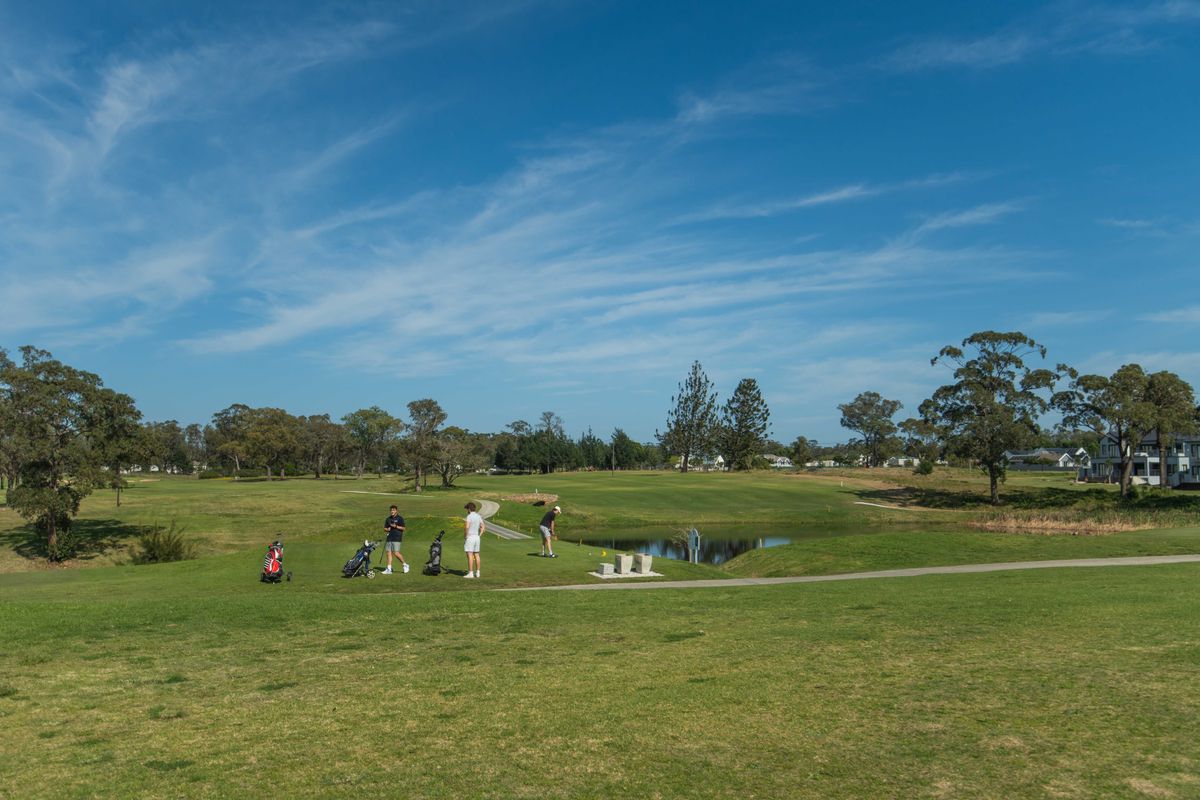 A scenic view of a well-maintained golf course featuring lush green fairways, mature trees, and a small water hazard.