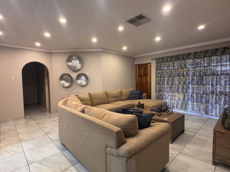 A spacious living room featuring tiled flooring, recessed downlighting, and a classic arched doorway leading to the hallway.